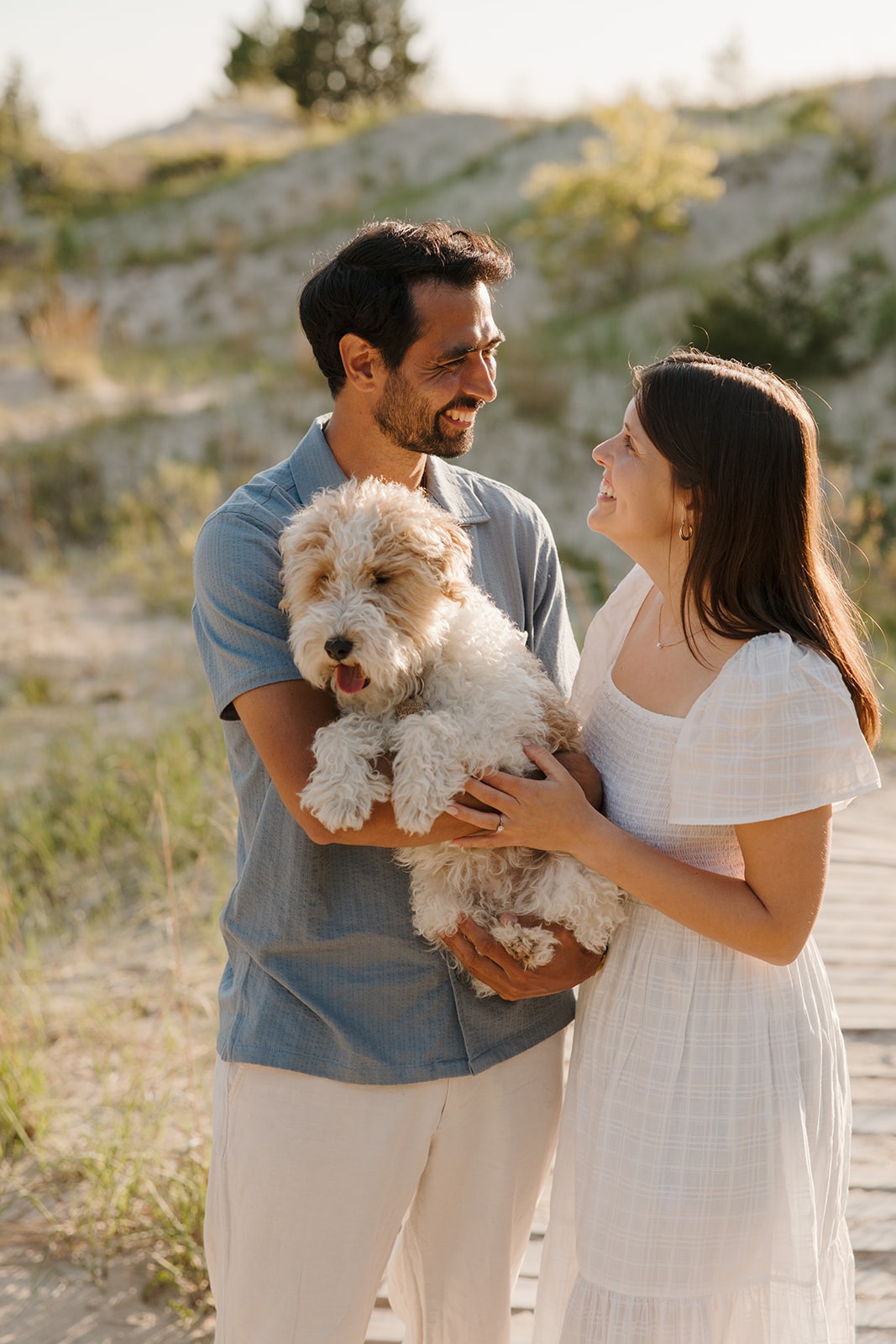 Sarah and Stephane smiling together while holding their dog.